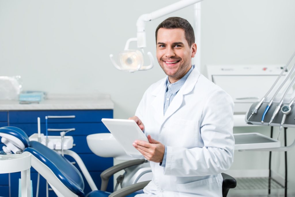 happy dentist in white coat holding digital tablet in dental clinic