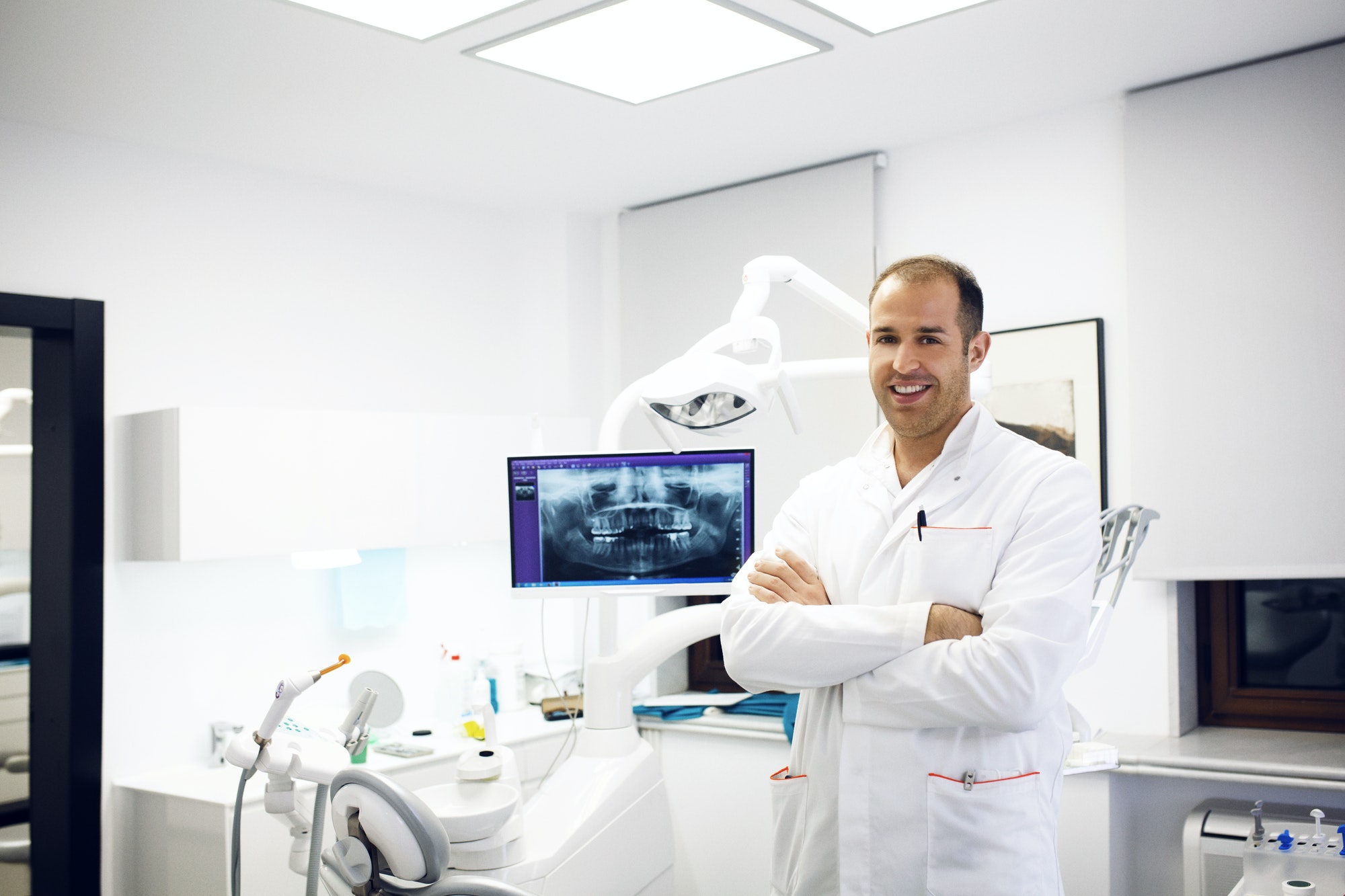 Portrait Of Confident Dentist Standing By Dental Equipment In Clinic